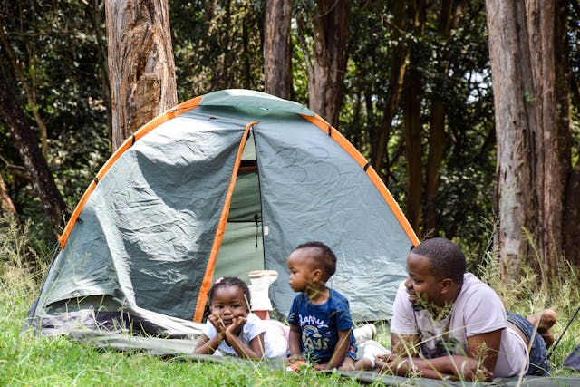 A man sitting with his two children in front of a camping tent