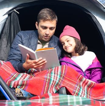 Dad reading to his daughter while they’re sitting in a tent