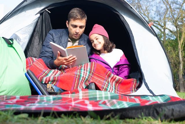 Dad reading to his daughter while they’re sitting in a tent