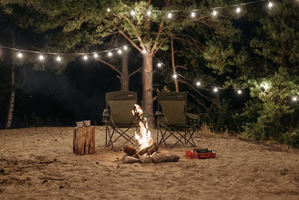 two camping chairs next to a fire, camping gear, cozy outdoors, fairy lights