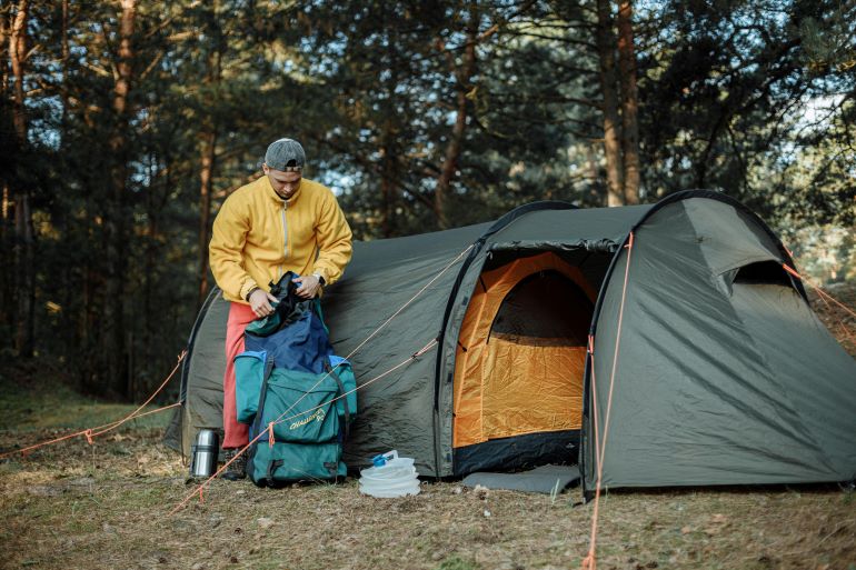 Camper unpacking gear next to a sturdy tent in a wooded campsite.
