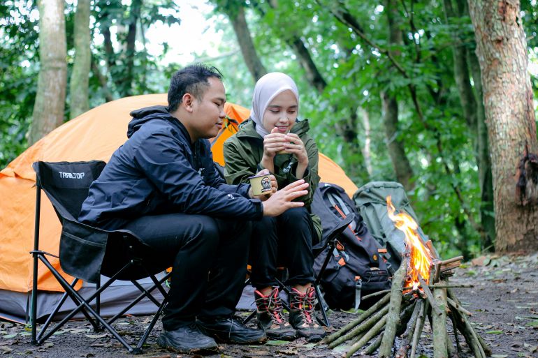 Campers sitting by a campfire near a tent in a forest.