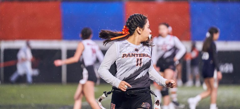 a young woman in sports attire plays flag football in the rain